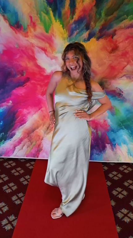 Prom queen in a formal gown posing on a red carpet in front of a colorful backdrop